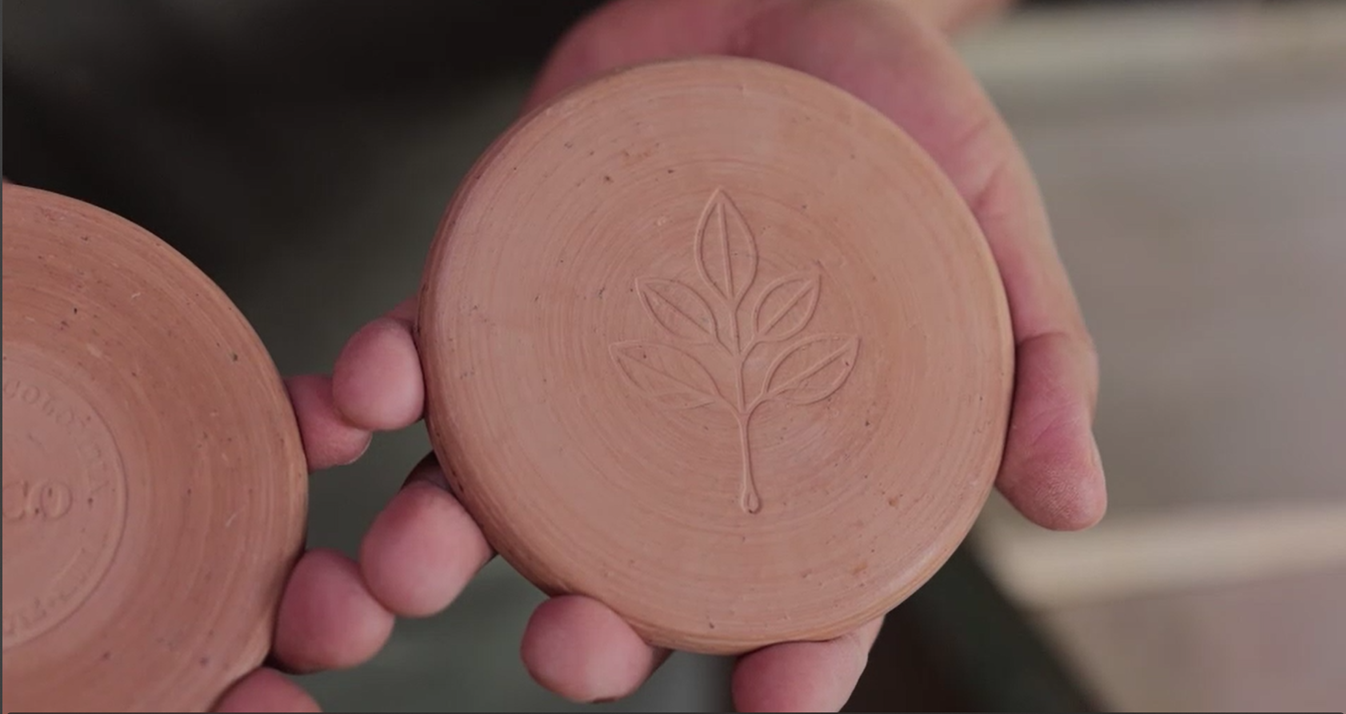 Person holding two terracotta pots with leaf design, blurred background